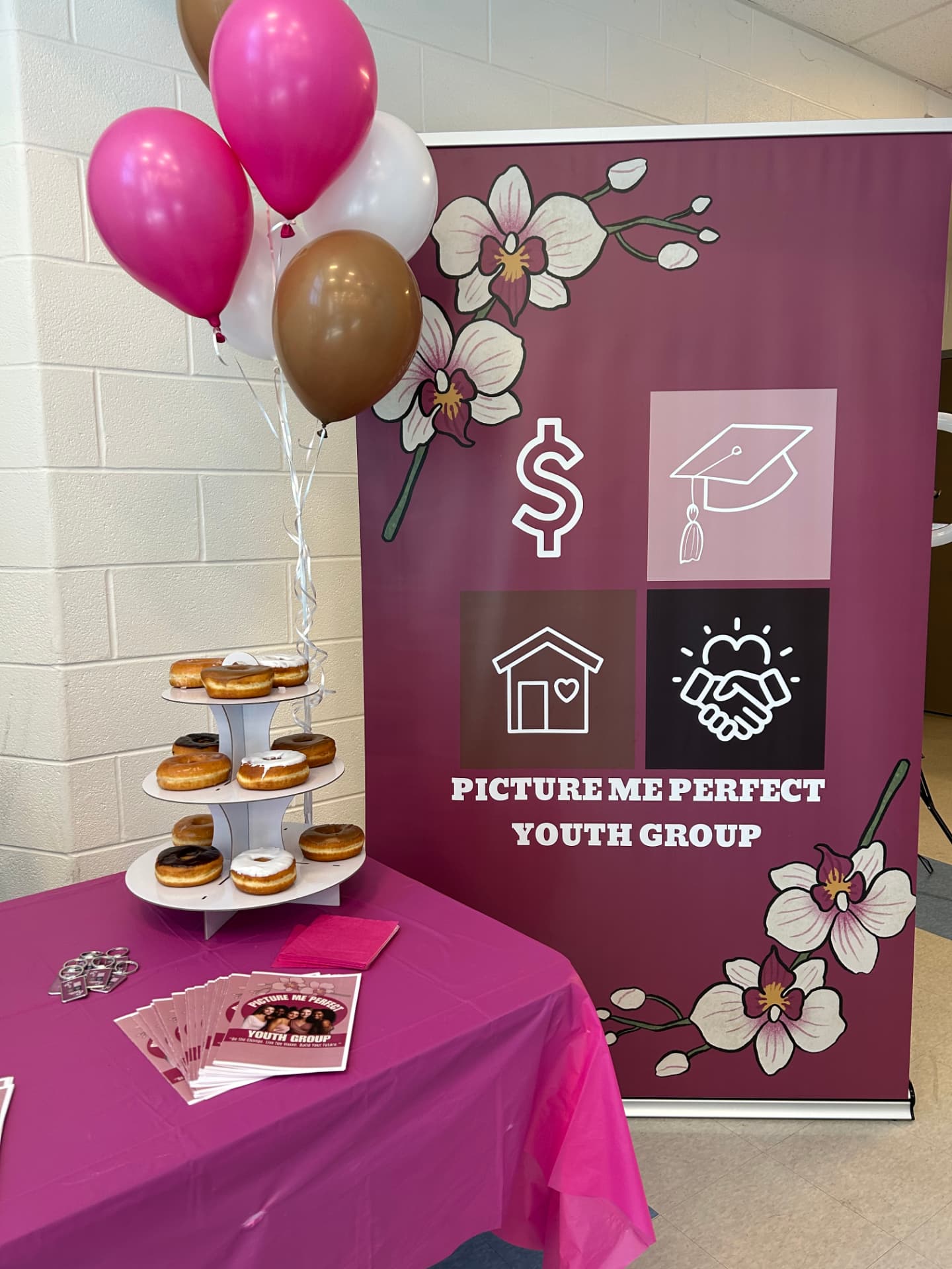 PMPYG event welcome table with pink balloons, donuts and flyers beside the berry orchid banner